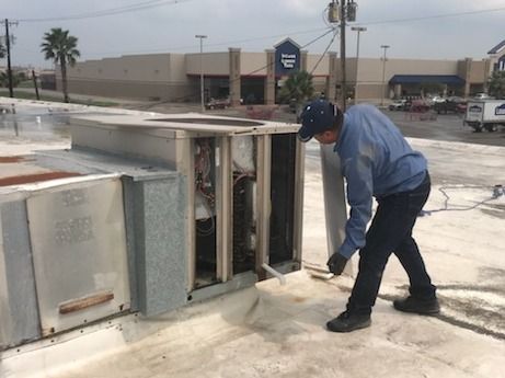 Worker inspecting a damaged utility box on a wet rooftop parking lot