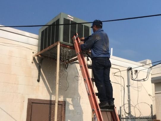 Worker on a red ladder servicing rooftop HVAC unit on a beige building