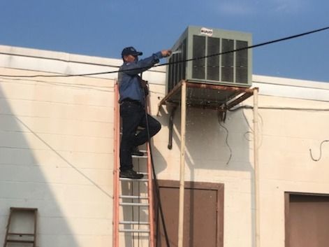 Technician climbing a ladder to service an air conditioner mounted on a wall outdoors