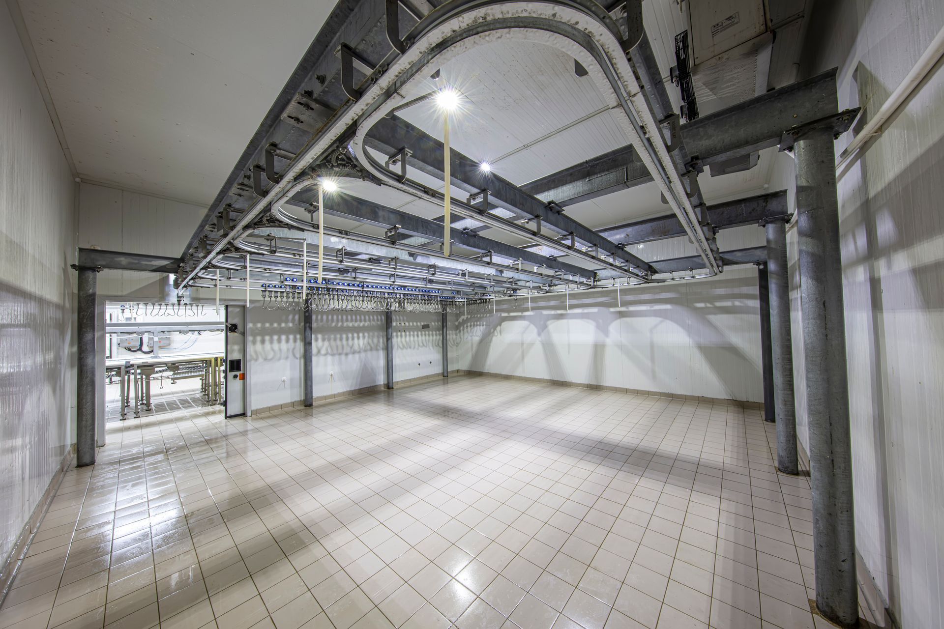 Empty industrial room with tiled floor, exposed ceiling ducts, and large windows