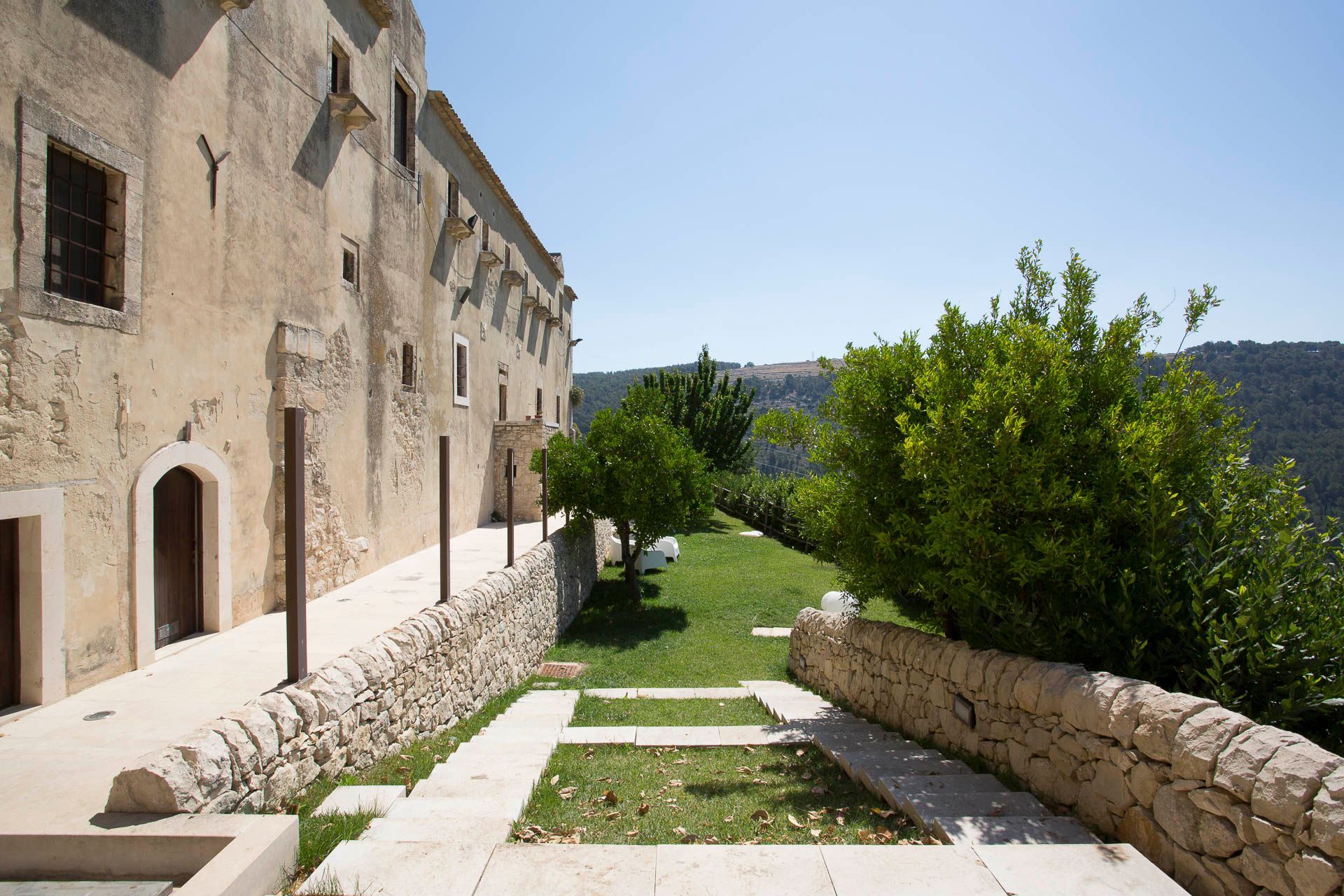 Un muro di pietra circonda un grande edificio con davanti un rigoglioso cortile verde | Antico Convento dei Cappuccini