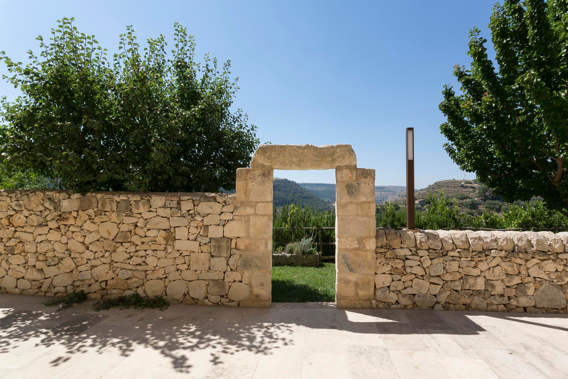 Un muro di pietra con una porta che conduce ad un rigoglioso campo verde | Antico Convento dei Cappuccini | Sicilia