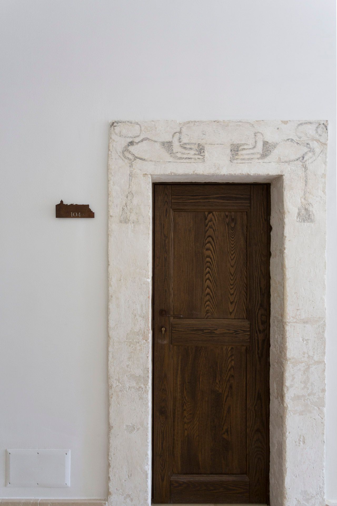 In una stanza con una parete bianca c'è una porta di legno con cornice in pietra. Hotel Ritiro con Vista all'Antico Convento.