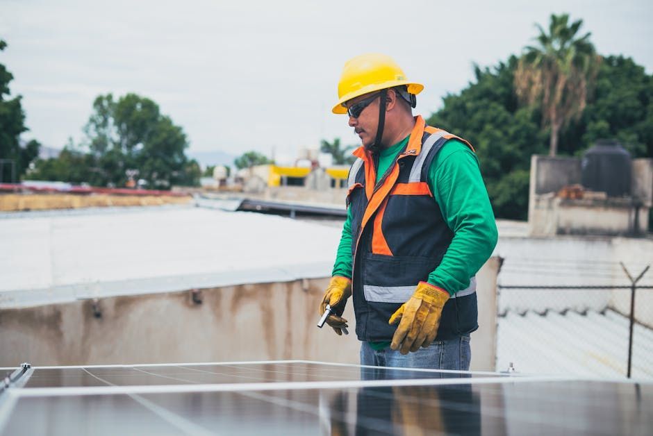 Construction worker in yellow hard hat and orange vest inspecting rooftop installation.
