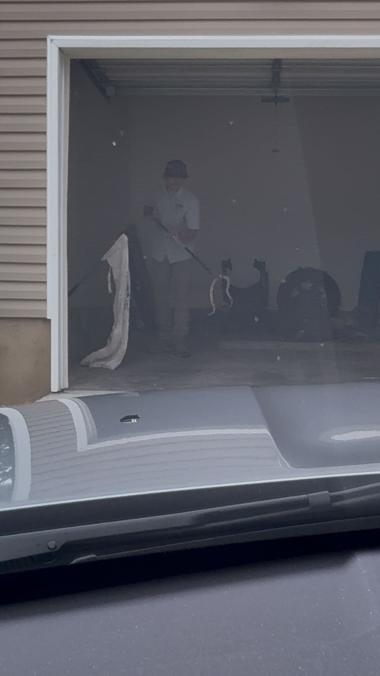 Person standing in a dim garage, seen through a partially open door from inside a car.