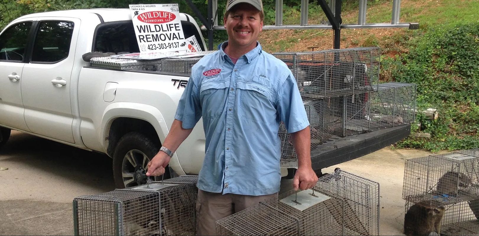 Man in blue shirt standing by white truck and metal cages outdoors with a sign in the truck window