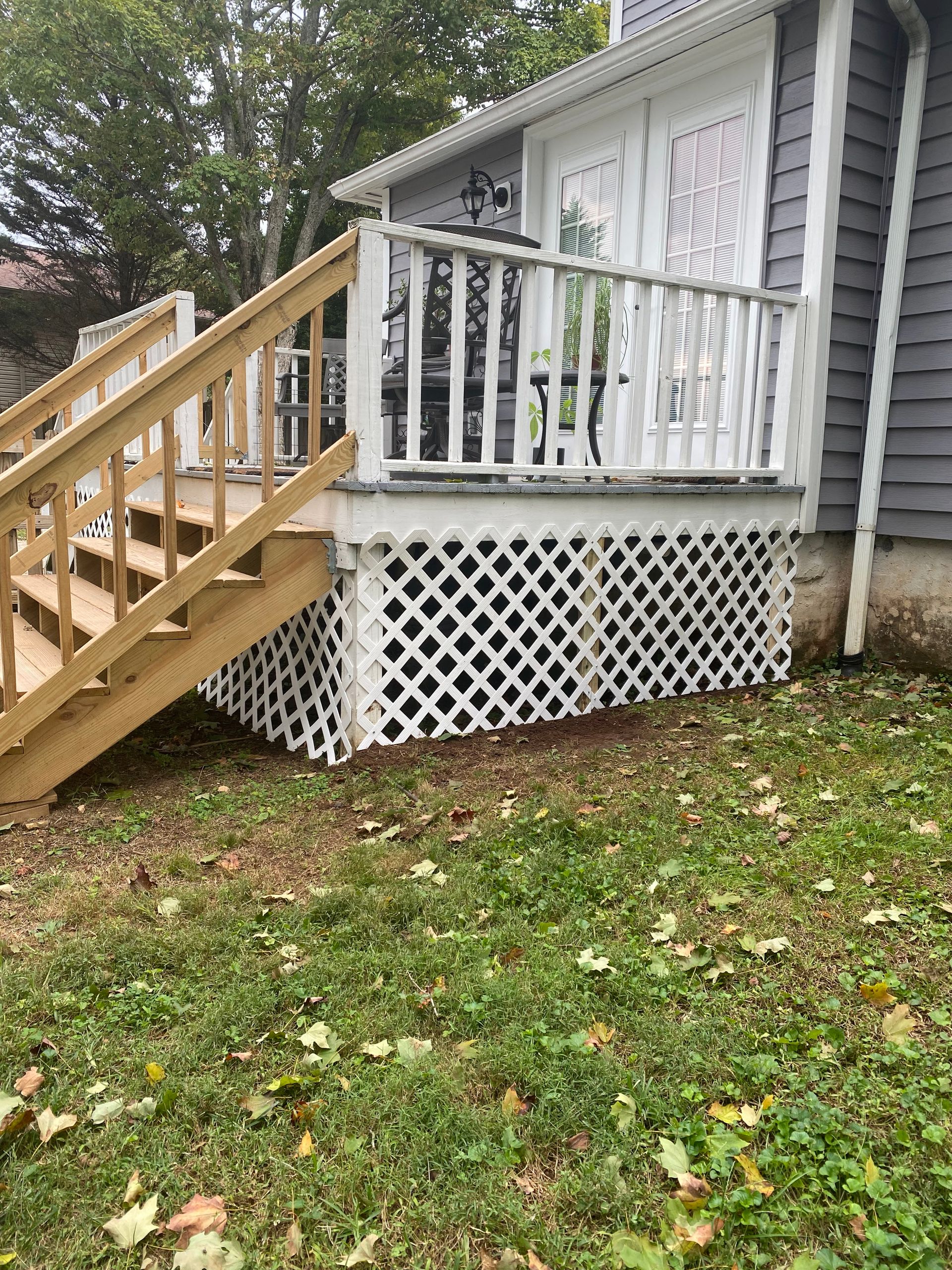 White porch with wooden stairs and railing beside gray house, over a white lattice foundation in a grassy yard