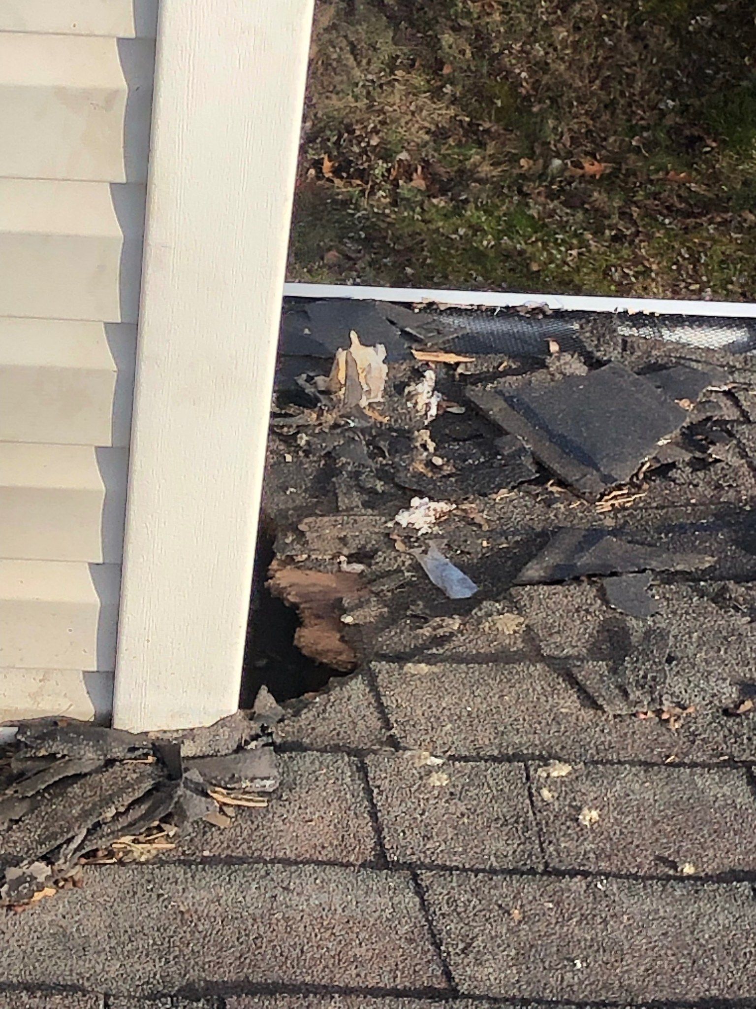 Damaged roof near a white chimney, with missing shingles and debris around the base.