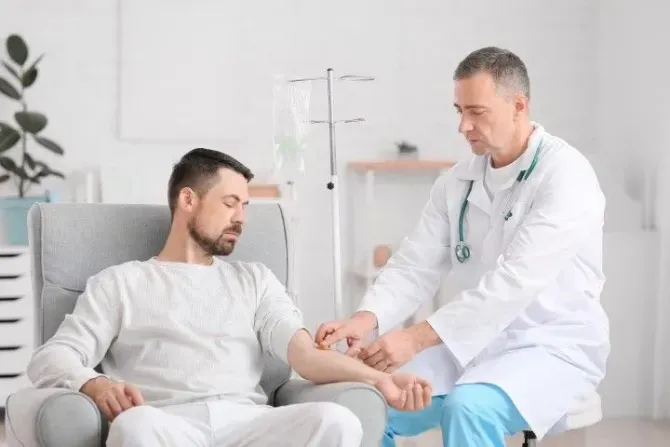 Medical professional inserting an IV into a man's arm in a bright office.