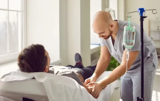 Male practitioner setting up an IV line for a patient on a clinic bed.