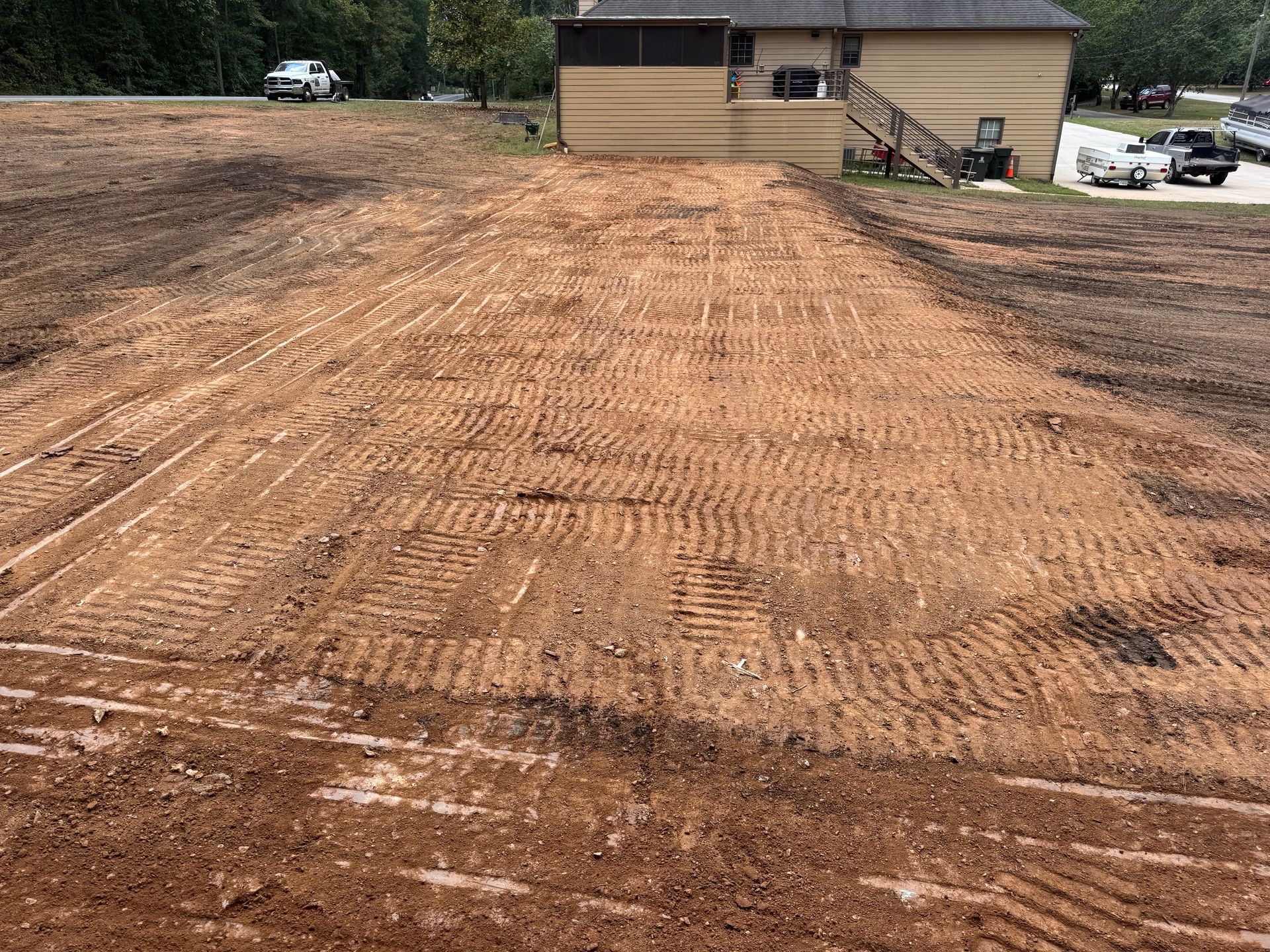 Brown dirt graded and leveled in front of a tan building; tire tracks across the dirt.