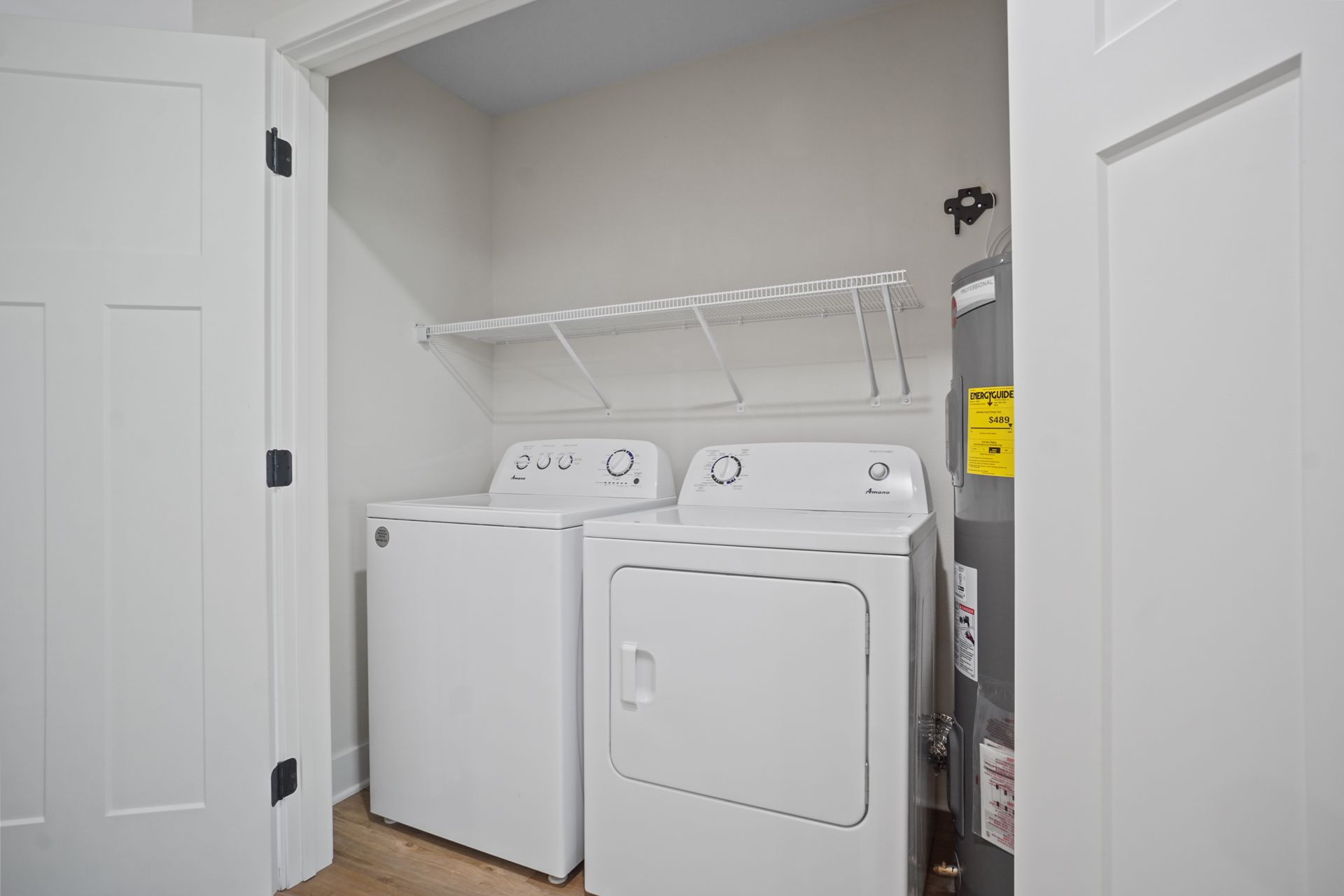 Laundry closet with a white washer and dryer under a shelf in a small alcove