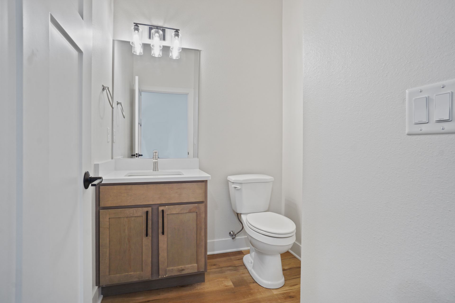 Small bathroom with wood vanity, sink, mirror, toilet, and white walls.