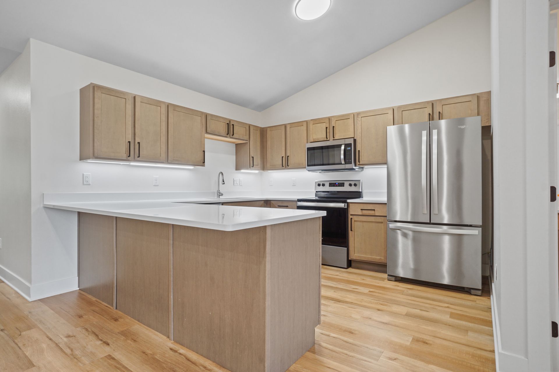 Modern kitchen with light wood cabinets, stainless steel refrigerator, and a white island counter