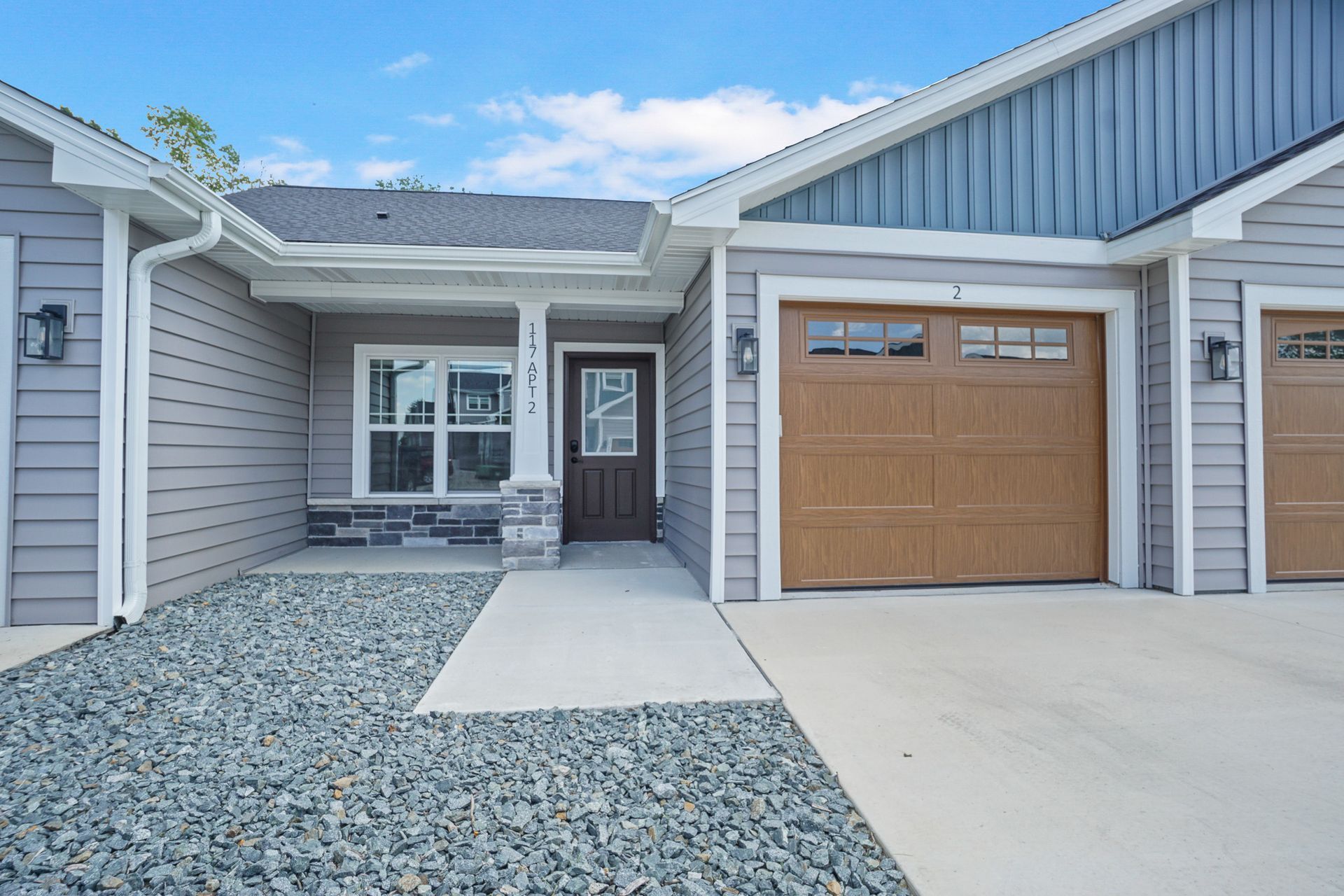Front entrance of a gray house with a wooden garage door, concrete driveway, and stone landscaping.