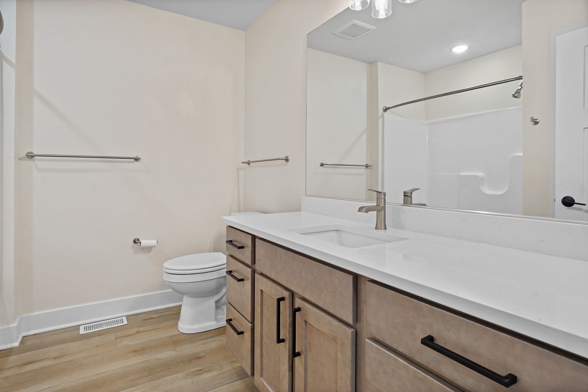 Modern bathroom with double vanity, large mirror, toilet, and towel bars on beige walls
