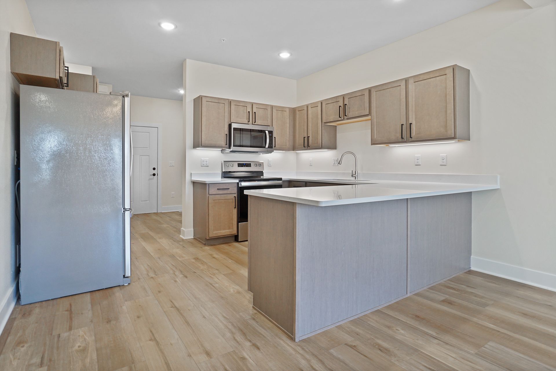 Bright modern kitchen with light wood cabinets, stainless steel appliances, and an island under recessed lights