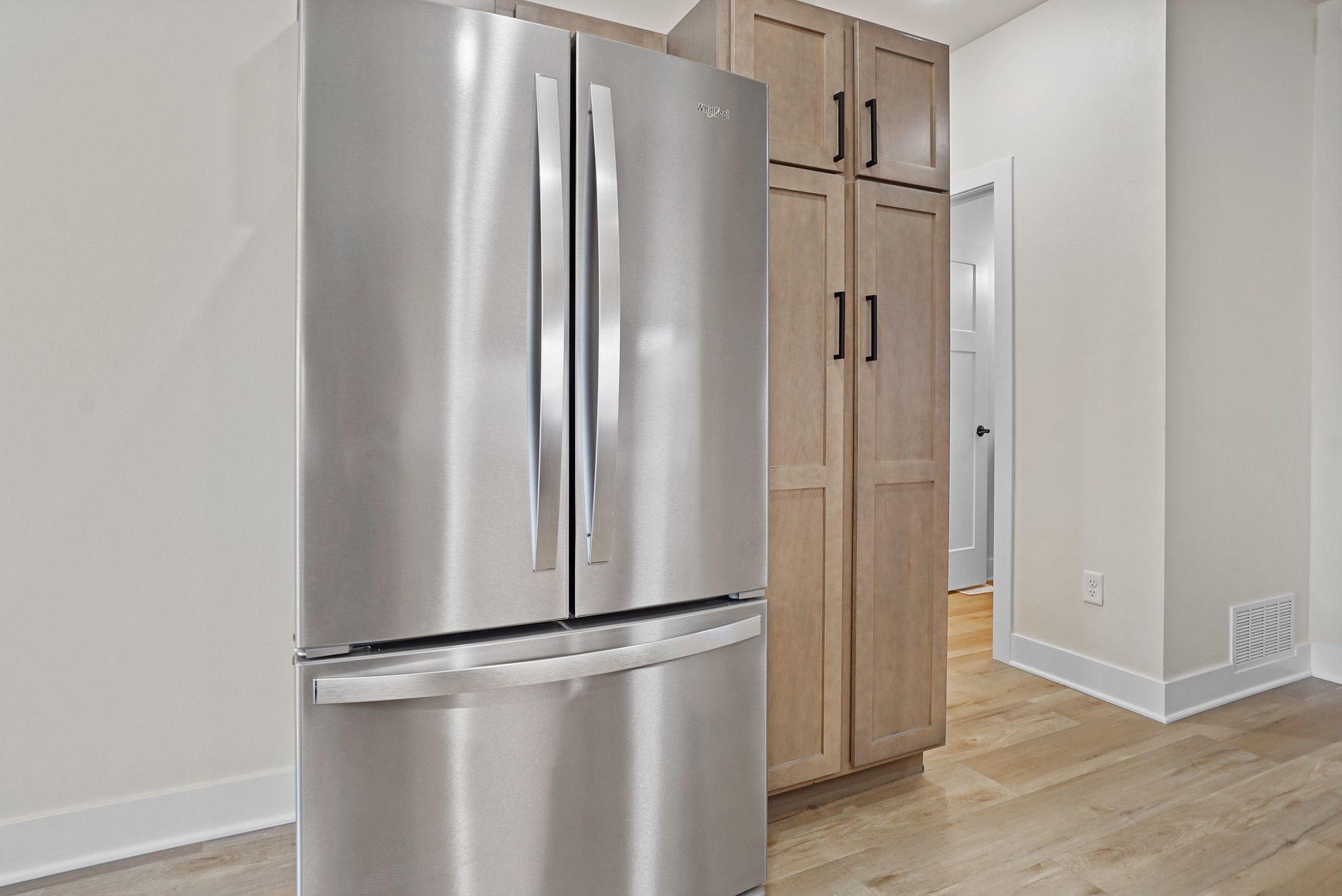 Stainless steel refrigerator beside a light wood pantry cabinet in a bright kitchen.