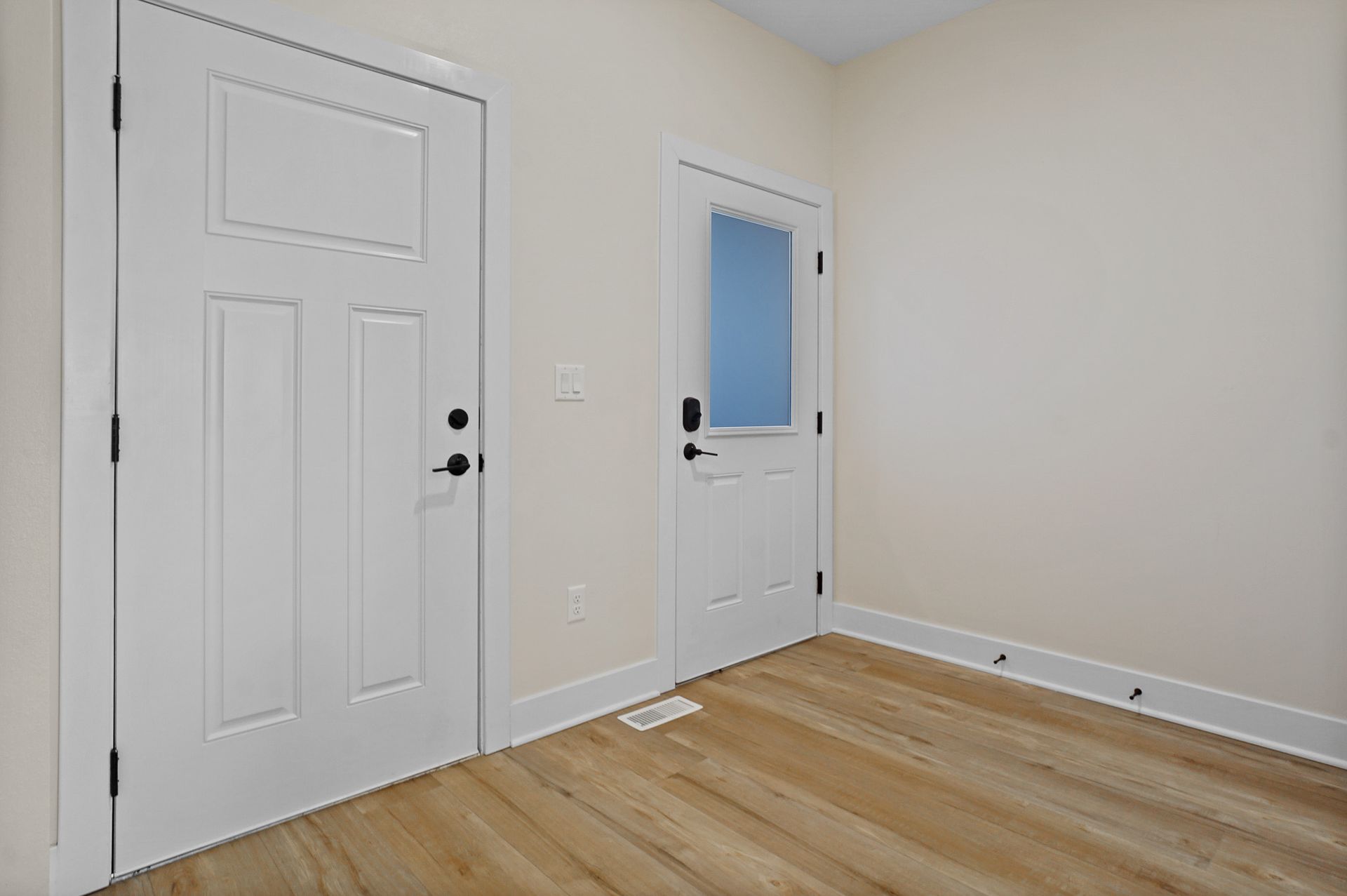 Empty white room with two doors, light wood floor, and beige walls.