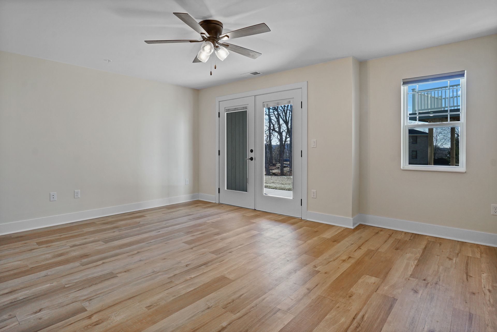 Empty living room with hardwood floors, ceiling fan, and French doors to a balcony.