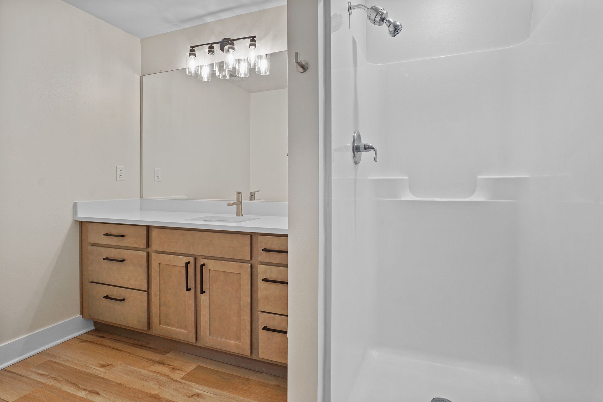 Bathroom vanity with wood cabinets, large mirror, and a white shower stall next to it