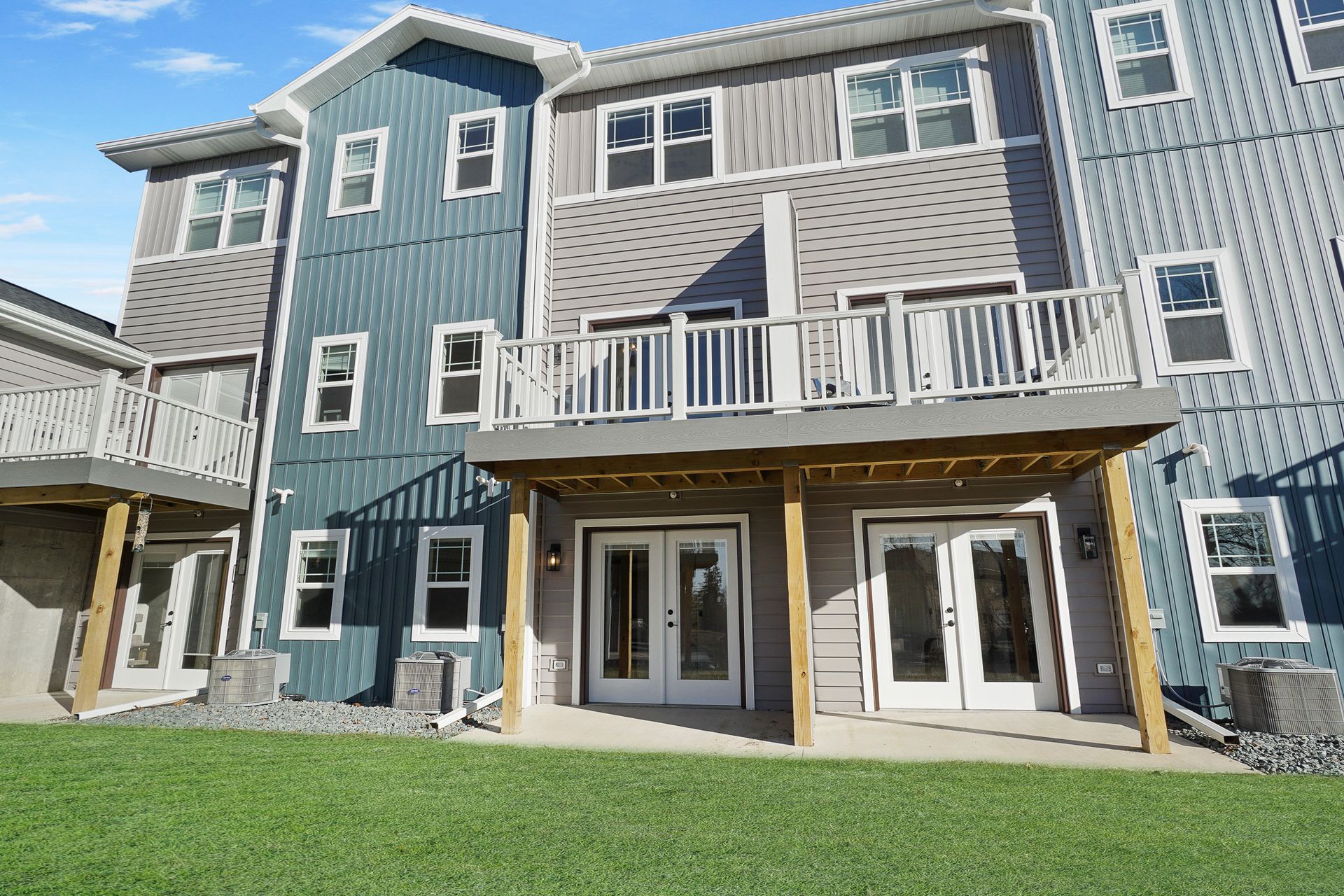 Multi-story blue and gray apartment building with white balconies and a grassy lawn