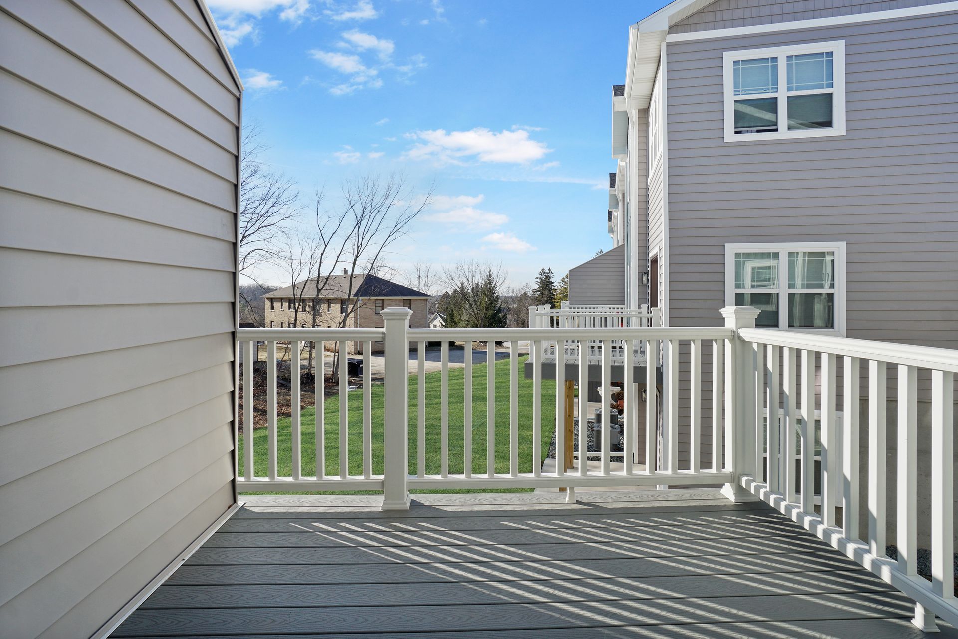 Back porch deck with white railing, overlooking a grassy yard and neighboring house on a sunny day