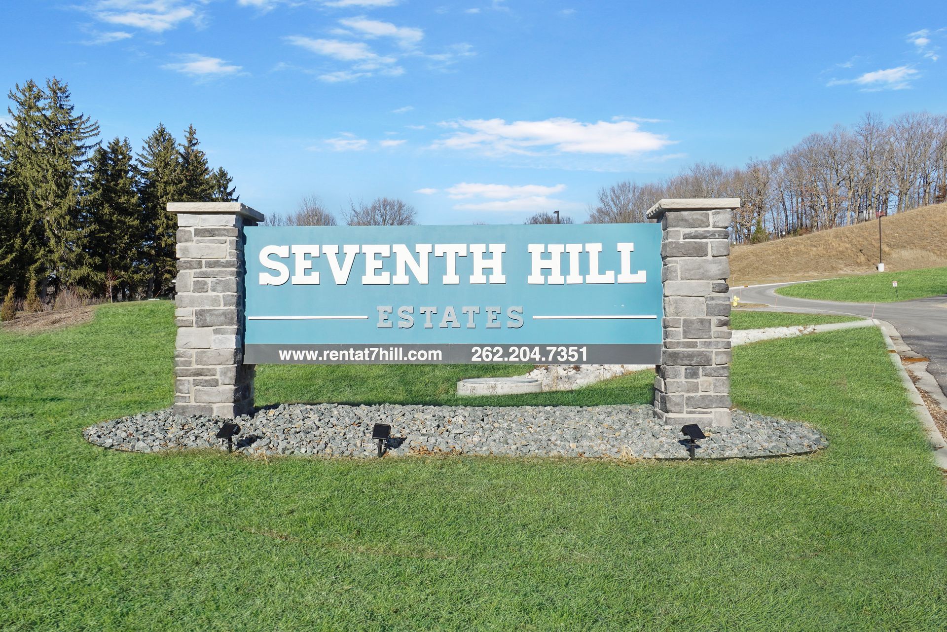 Seventh Hill Estates entrance sign on a grassy roadside under a blue sky