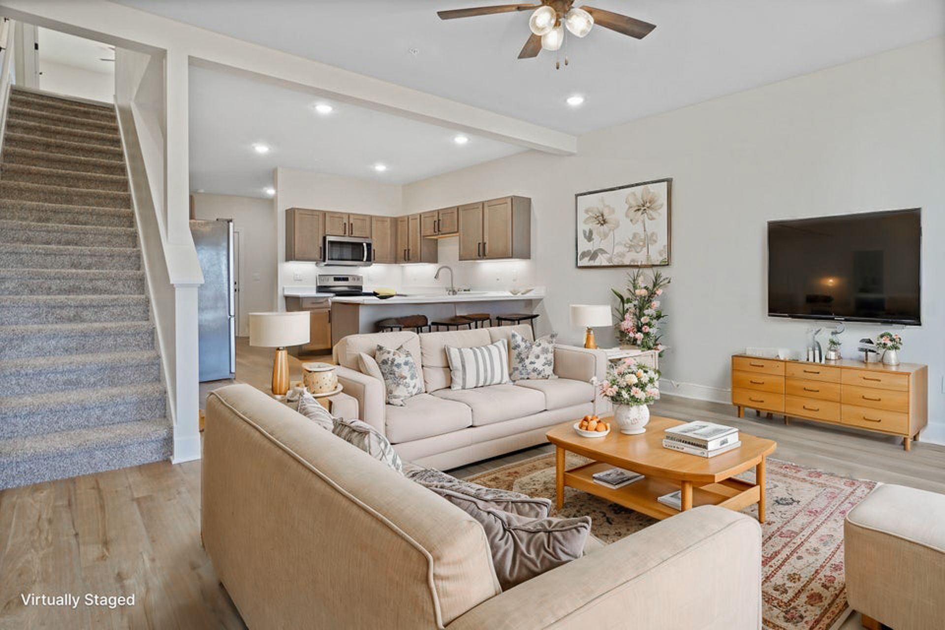 Bright open-concept living room with beige sofas, wood coffee table, TV, and kitchen in the background