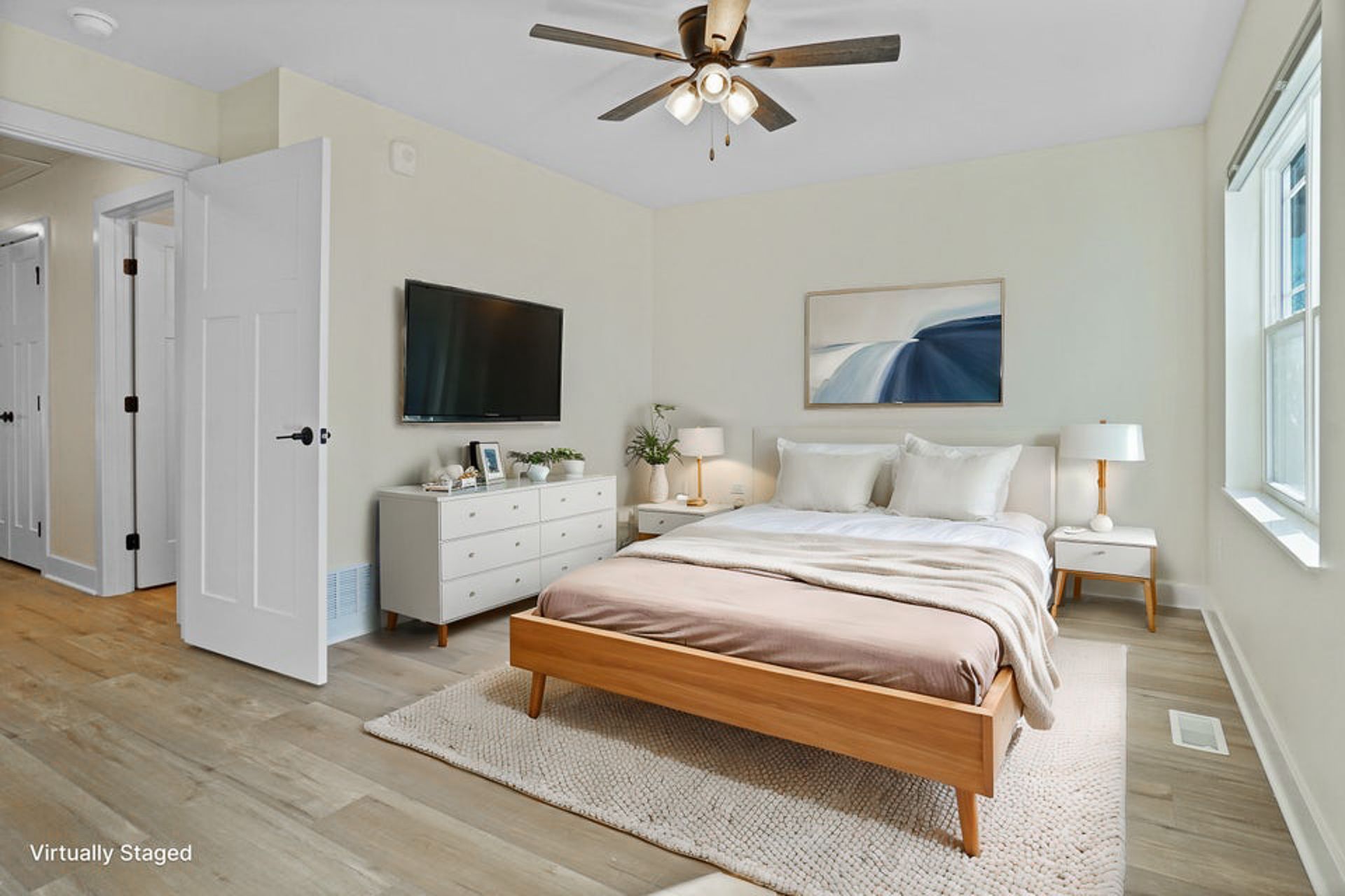 Bright bedroom with a wooden bed, dresser, wall-mounted TV, and large windows.