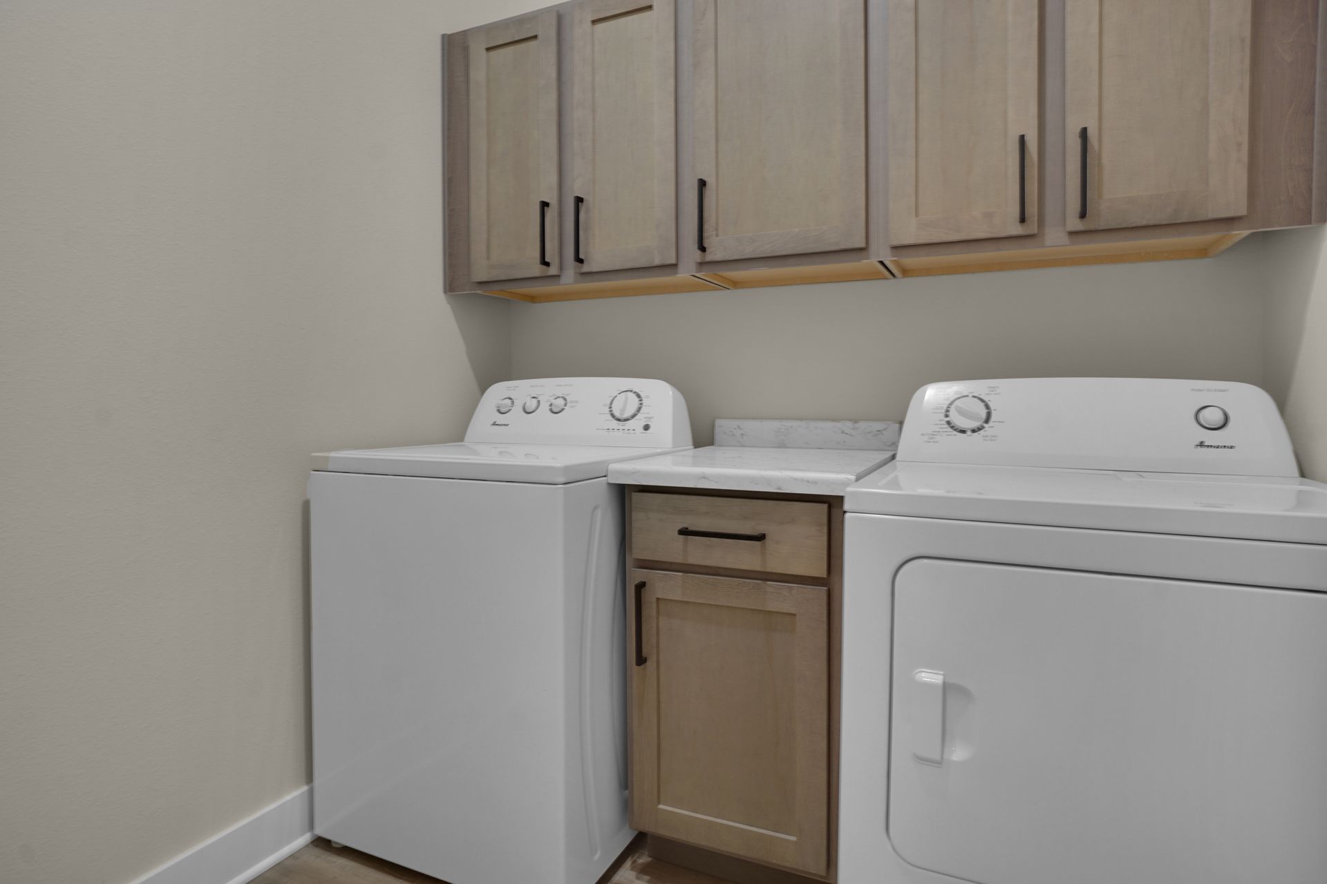 Laundry room with white washer and dryer under wood cabinets and a small center cabinet