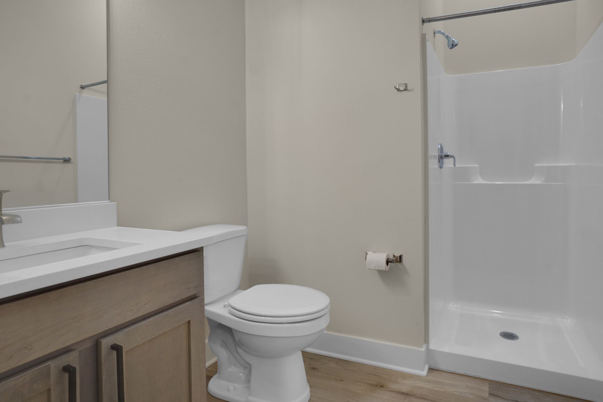 Small bathroom with vanity, toilet, and white shower/tub surround with gray walls and wood-look floor.