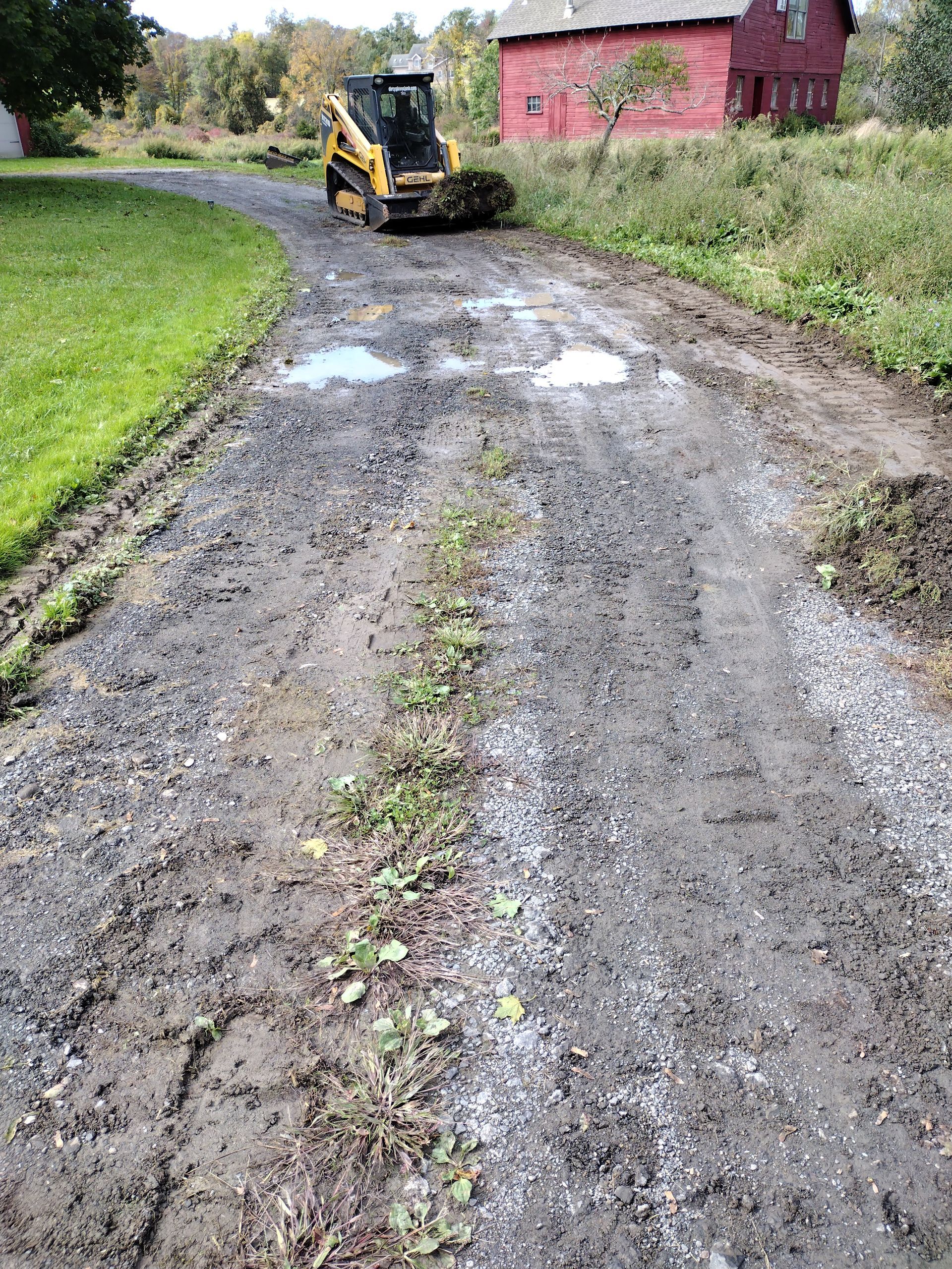Yellow skid steer clears gravel driveway; red barn in background.