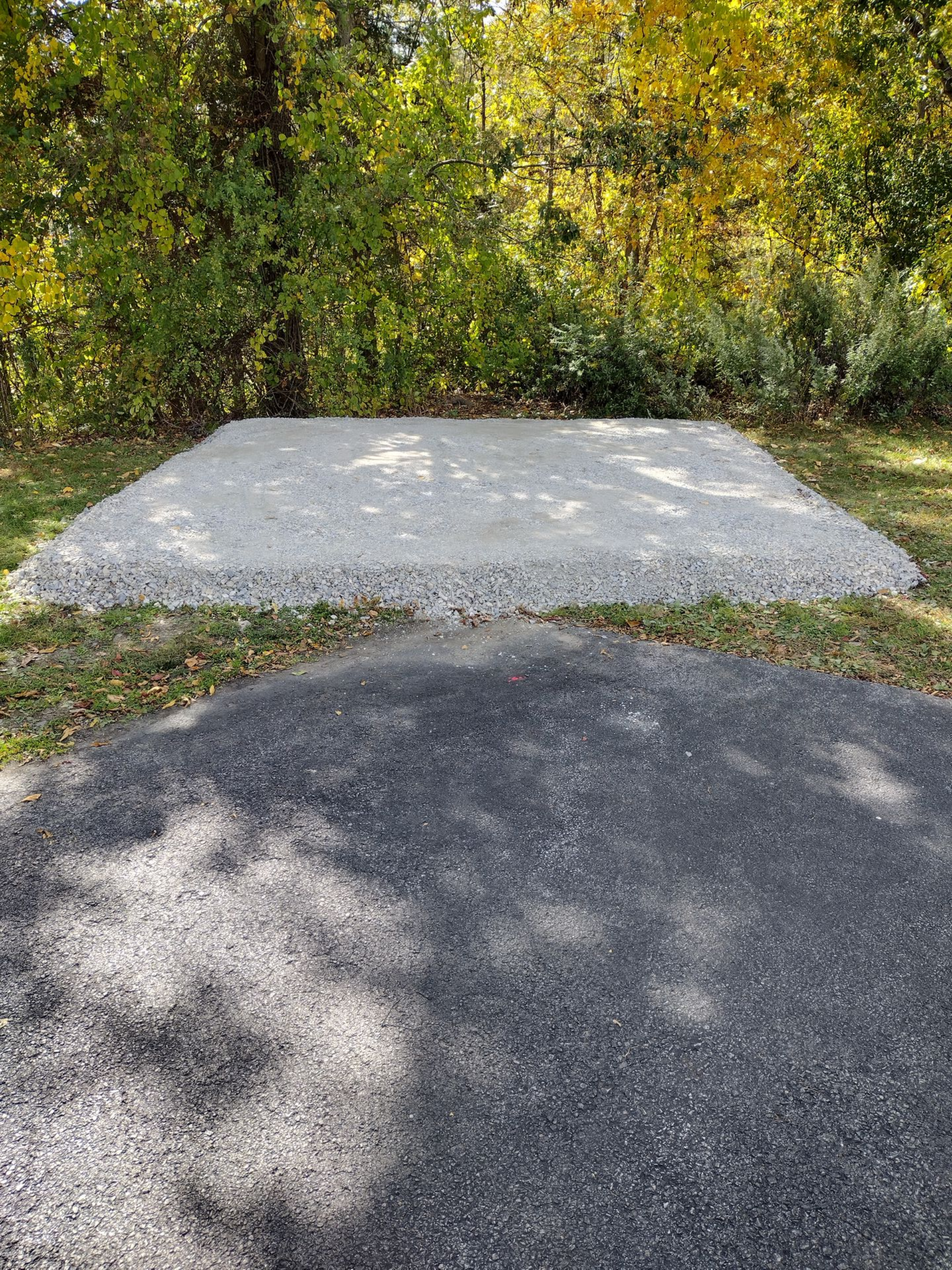 Gravel pad above asphalt parking area in a wooded setting.
