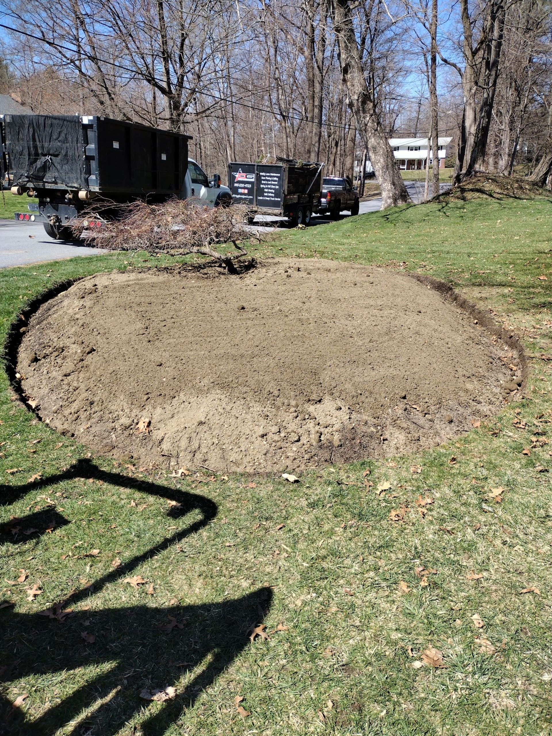 A cleared garden bed in grass with a tree chipper, truck, and trailer in the background.