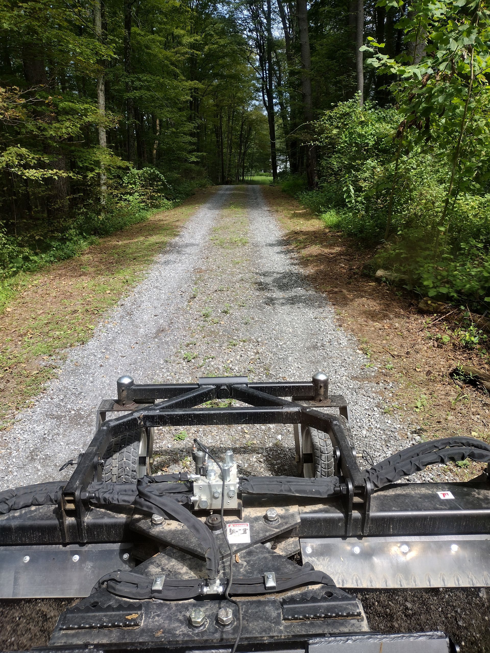Gravel road through a forest being graded by a tractor with a blade.
