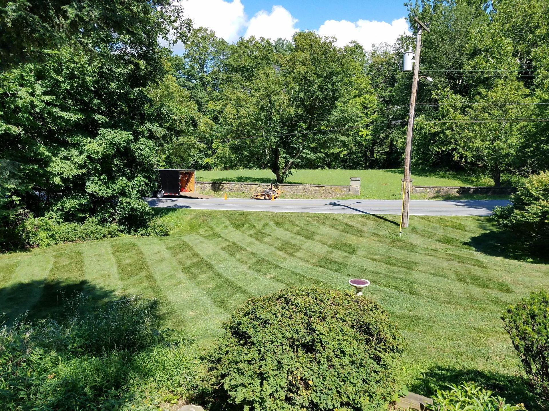 Lawn with patterned stripes, a road, trees, and blue sky.