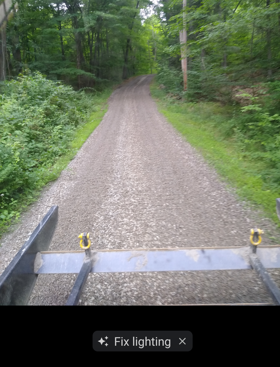 A gravel road through a green forest, viewed from behind a trailer.