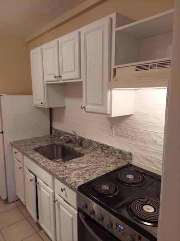 A kitchen with white cabinets , a stove , a sink and a refrigerator.