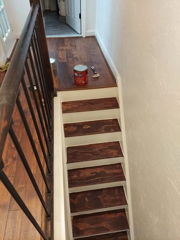 A wooden staircase with a metal railing and a can of paint on the floor.
