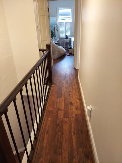 A hallway with hardwood floors and a railing leading to a living room.