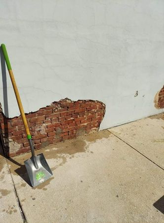 A shovel with a green handle is leaning against a white wall