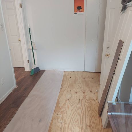 A hallway with a broom and a piece of plywood on the floor.
