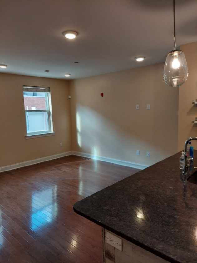An empty living room with hardwood floors , a sink , and a window.