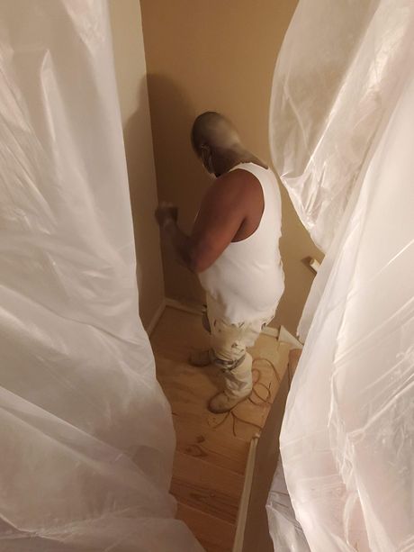 A man is painting a wall in a room covered in plastic.