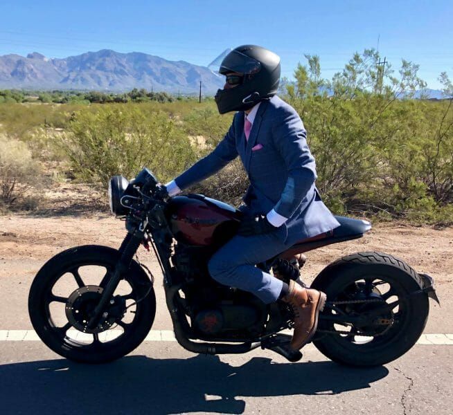 A man in a suit is riding a motorcycle down a road