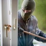 A man in a mask is breaking into a house with a crowbar.