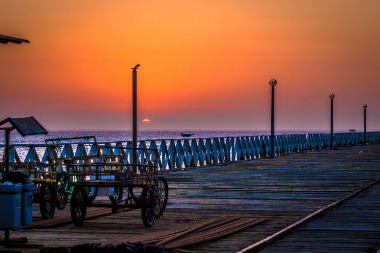 A pier with a sunset in the background and a row of carts on it.