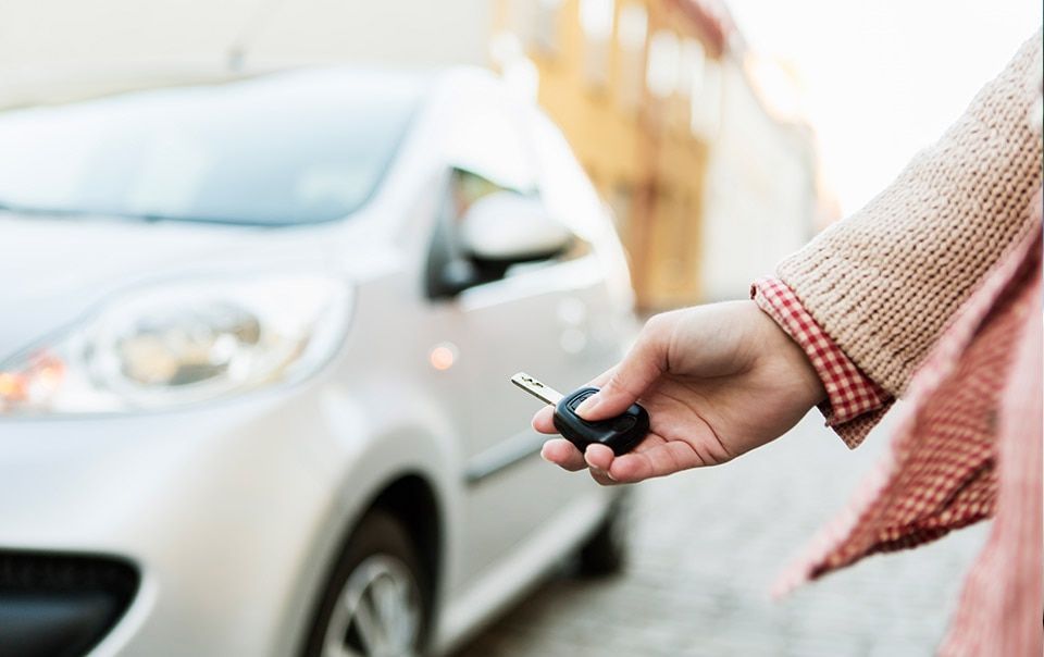 A person is holding a car key in front of a car.