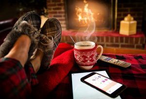 A person is sitting in front of a fireplace with their feet up and a cup of coffee.
